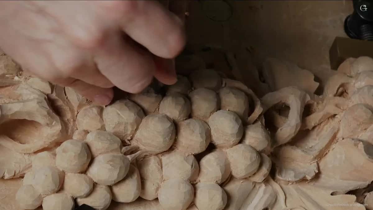 Hand at work among the fruit, the little finger down on solid carved surface