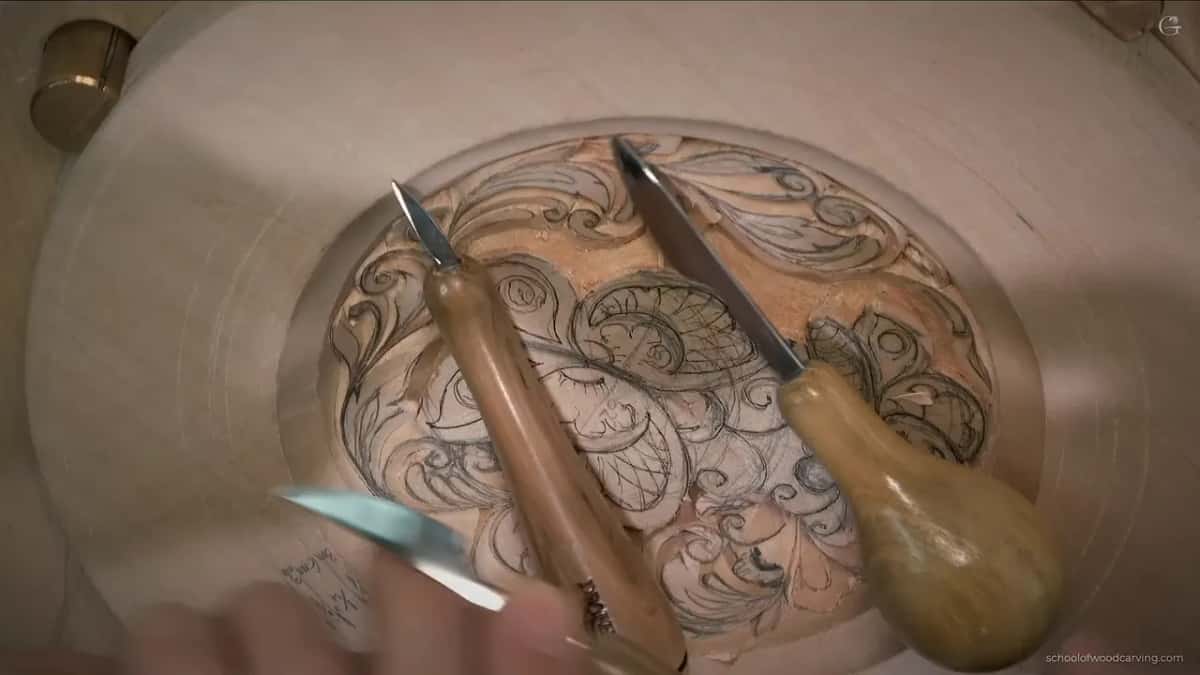 Two knives lie across the half-carved plate while a hand at the left holds up a small silver blade