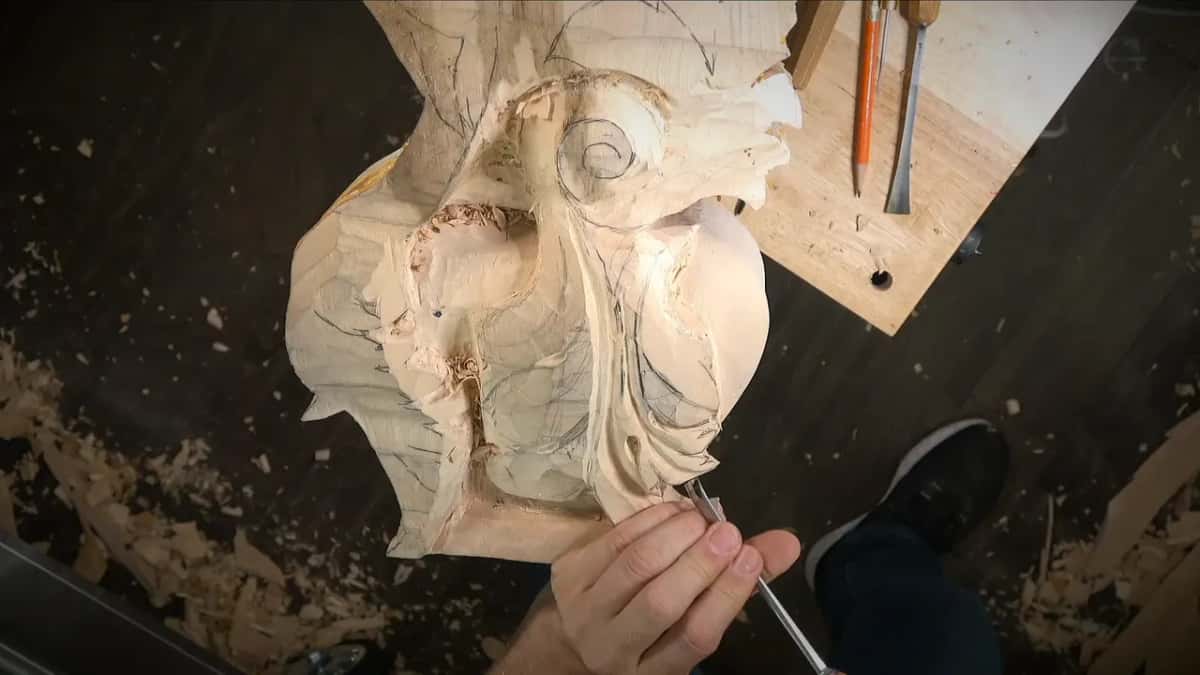 The whole corbel from above, with its scroll at the top, while a gouge works along its lower edge