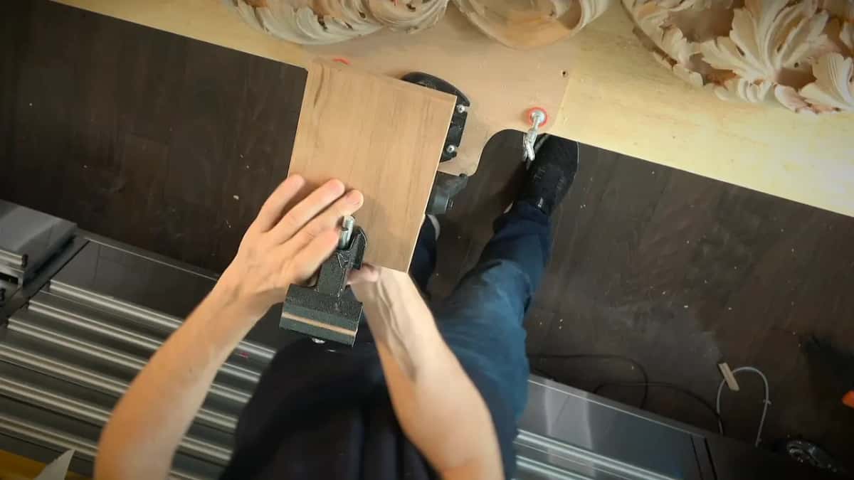 Both hands on the little clamp vise fixed to one end of a board