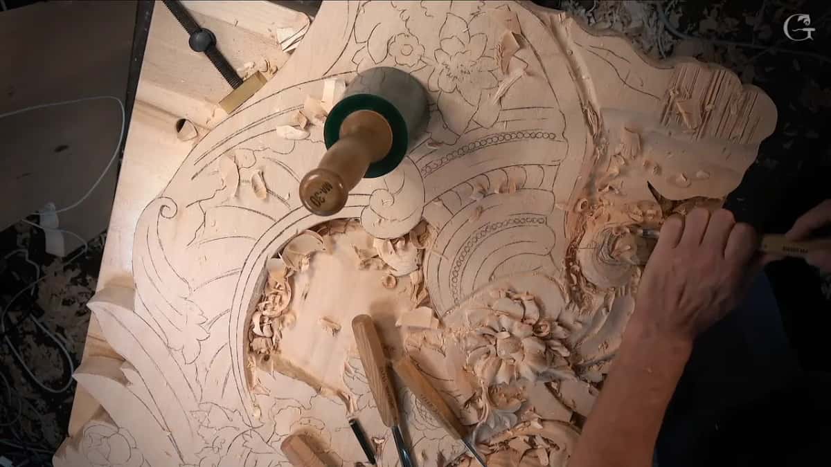 Whole panel seen from above, a mallet standing on the drawing, gouges lying below and one hand carving at the right