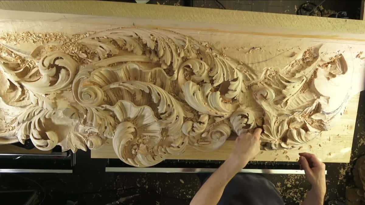 Two hands carving deep into a Venetian panel of scrolls, shells and acanthus