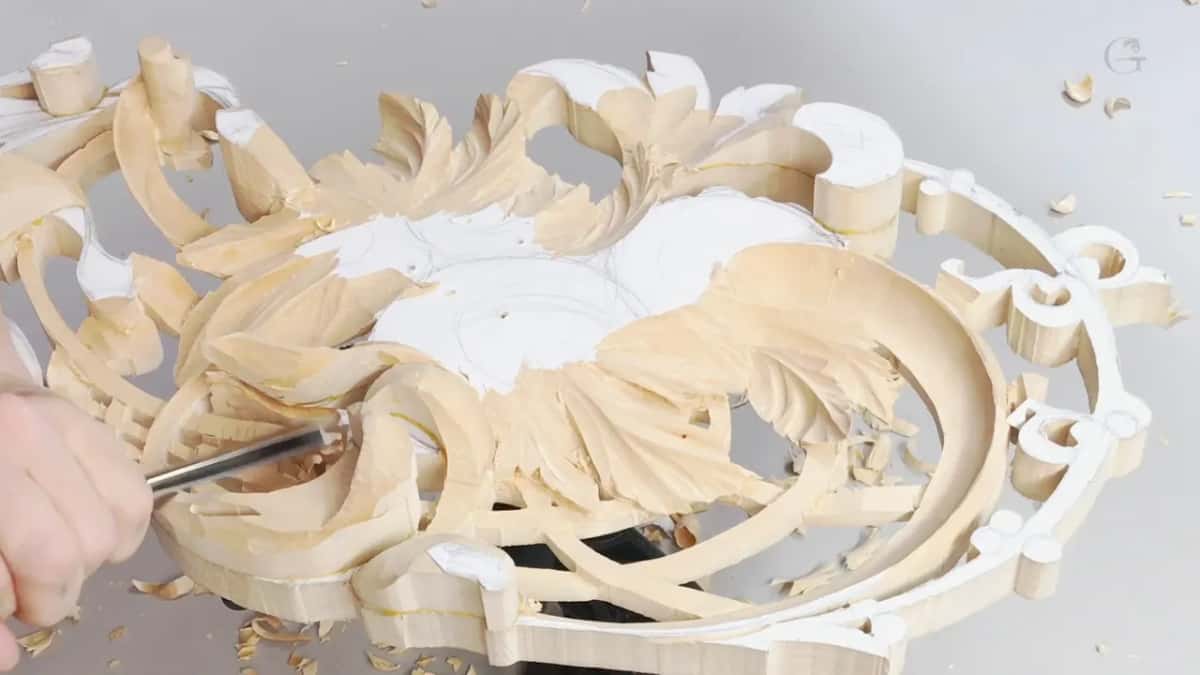 A gouge cutting acanthus on a pierced oval frame, white paper pattern still stuck to the blank
