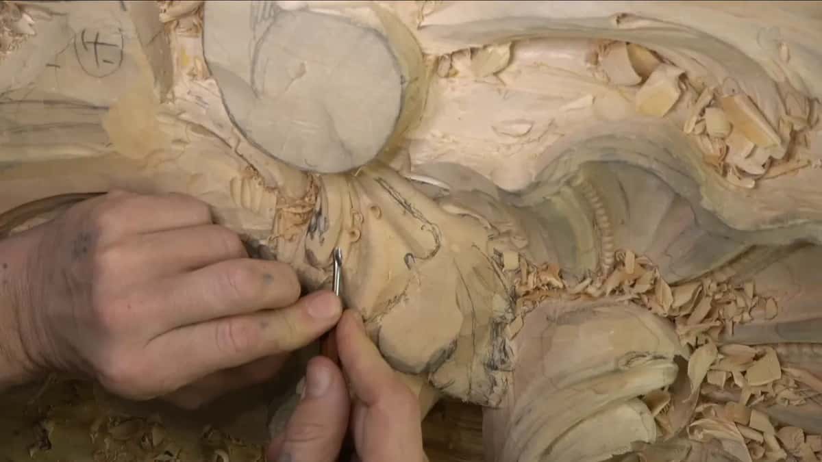 Thumb and fingers pinch a very narrow gouge against the edge right below the round pencil-marked boss.