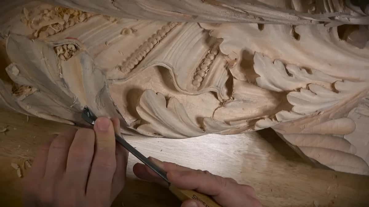 Two hands hold a narrow tool at the rim of a carved leaf, beaded molding to the right