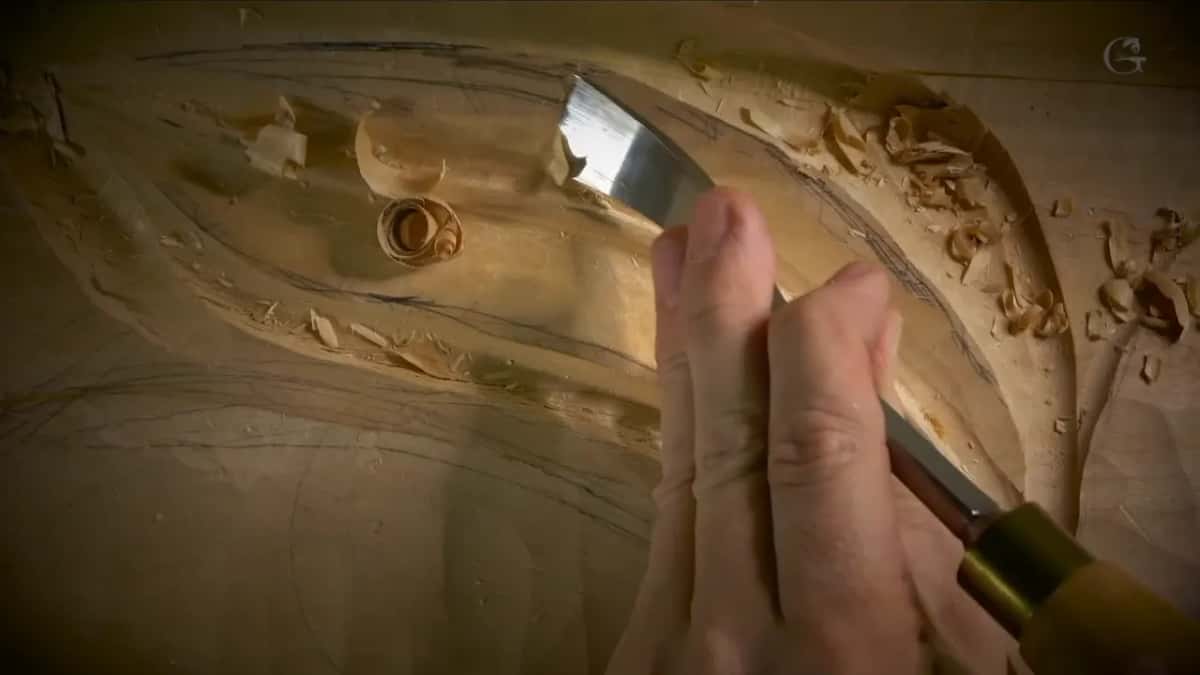 Wide blade with a brass ferrule, pushed by two fingers up a slope drawn in pencil, chips scattered across the top