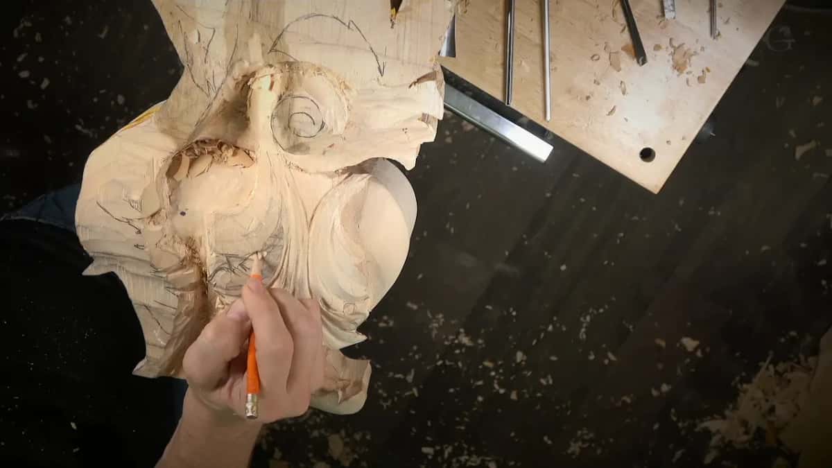 An orange pencil works among the lobes, gouges lying on a board above