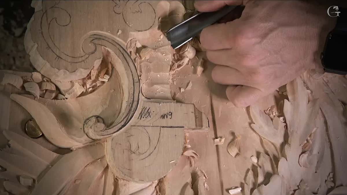 Close in, a tool cleans the wood just outside the volute, with the pencil note still showing