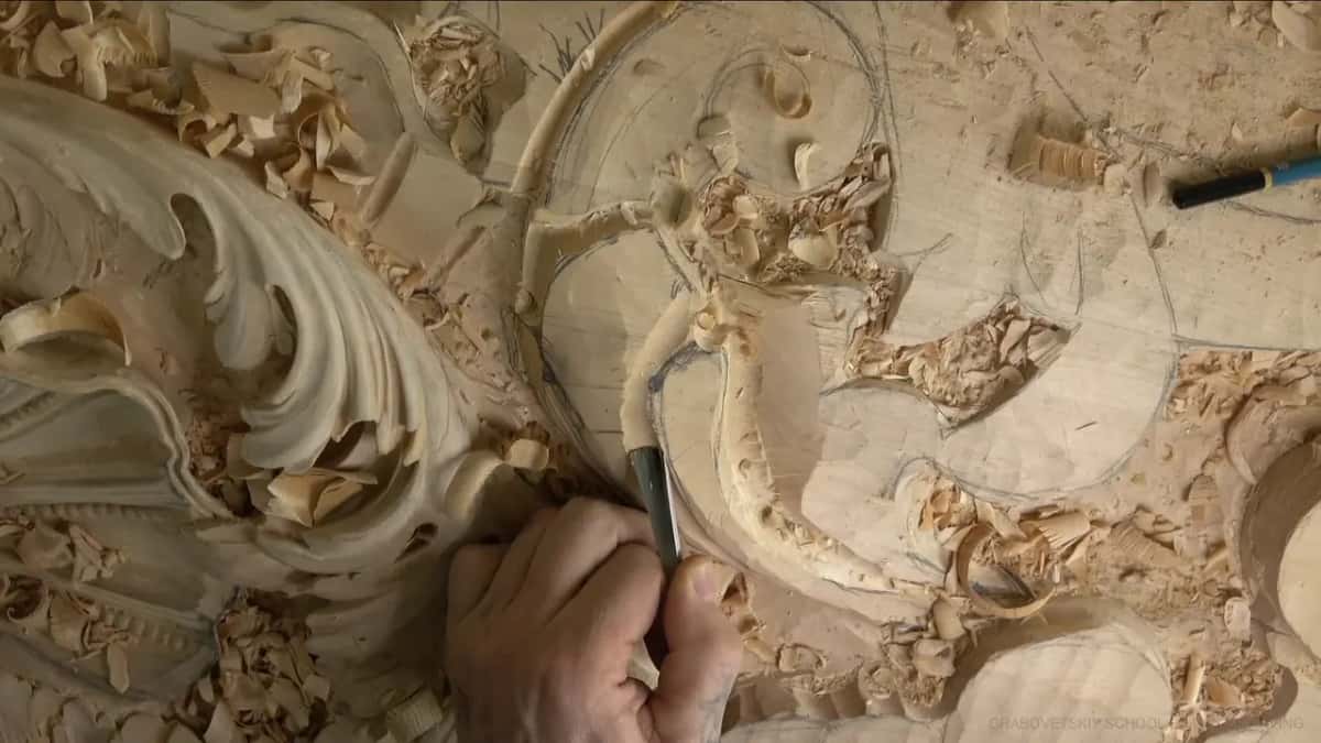 A gouge carves a hollow beside a long curved ridge while a blue marker lies on the flat wood nearby.