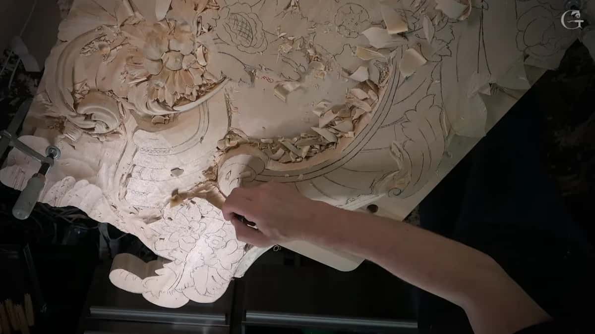Hand following the redrawn pencil lines beside the finished scroll, with the clamp at the far left of the bench