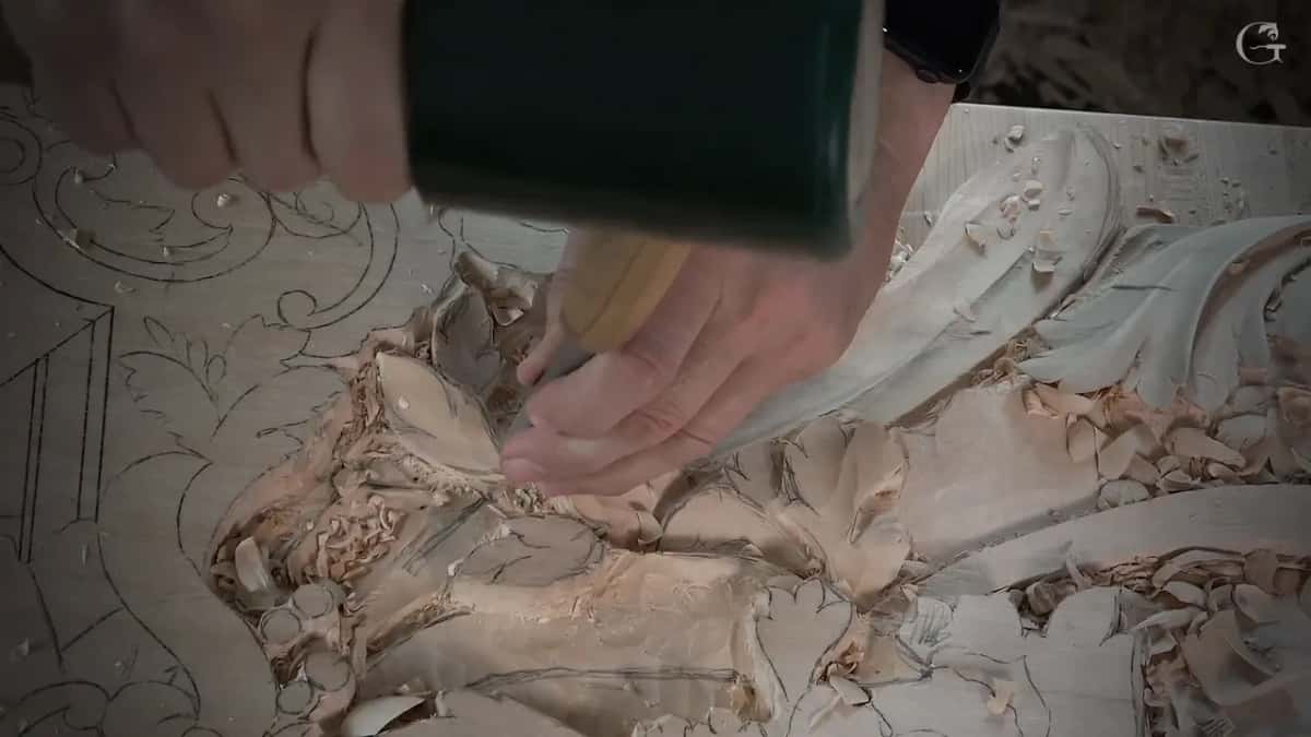 Green mallet above the handle of a gouge that sits in a small leaf, with scroll lines drawn behind