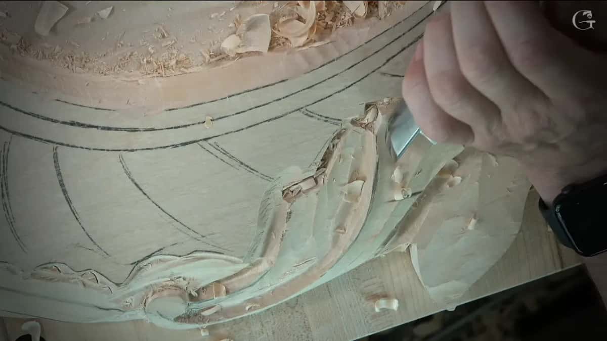 From a low camera angle, the gouge runs along the carved edge with curved pencil bands of the frame behind