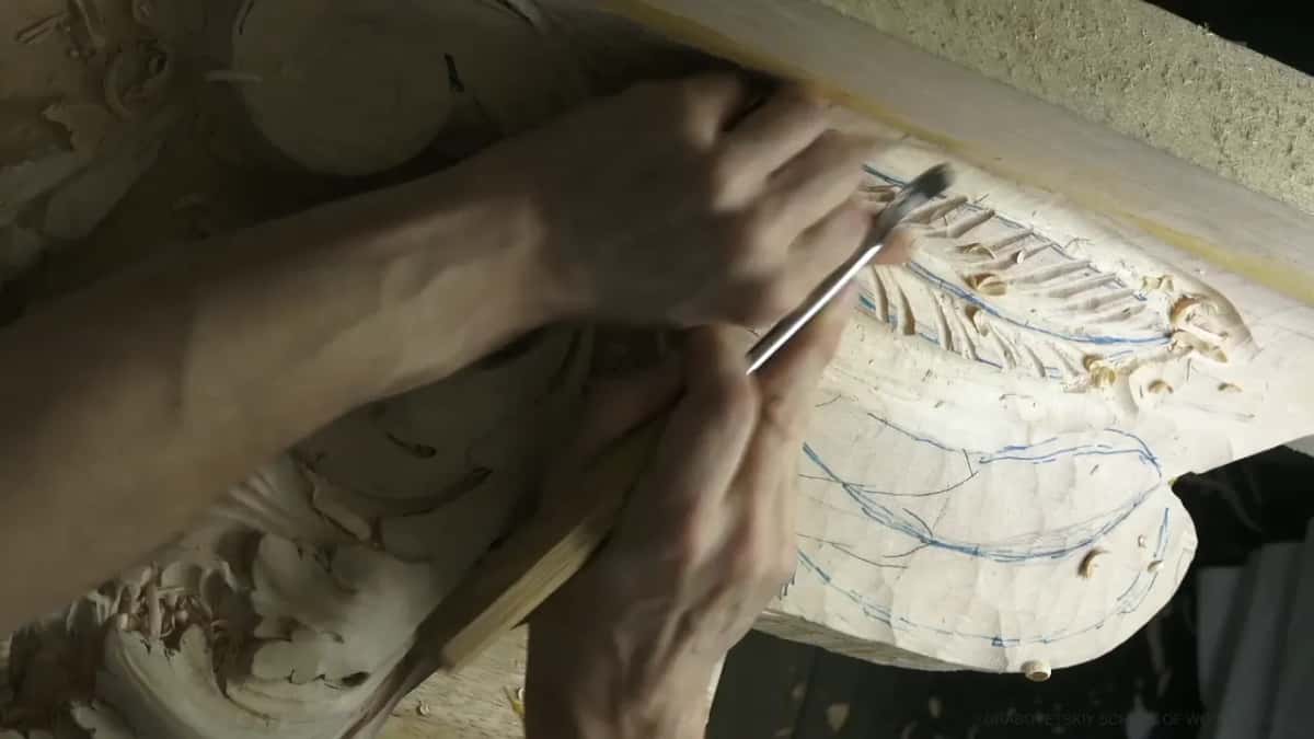 An arm stretches across the carving, the tool at the ribs near the far edge.