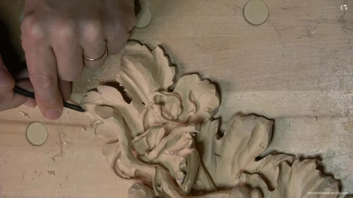 Hand steady on finished carving while a small gouge works the hollow inside a fold