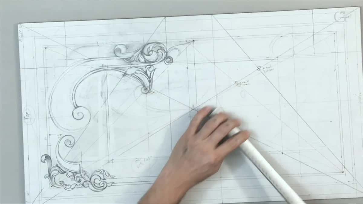 One hand presses a long white stick onto the lines right of the scrolls
