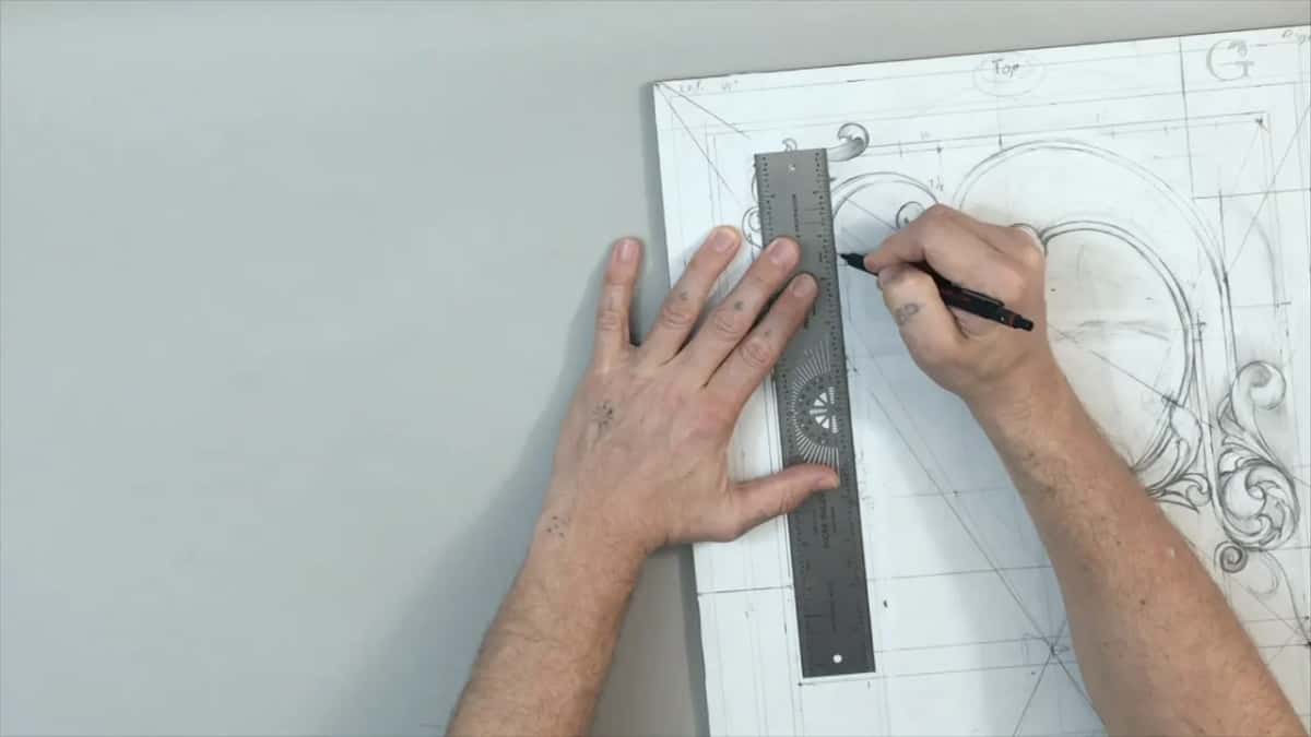 Left hand pins a steel rule flat near the top while the right draws beside it with a black pencil