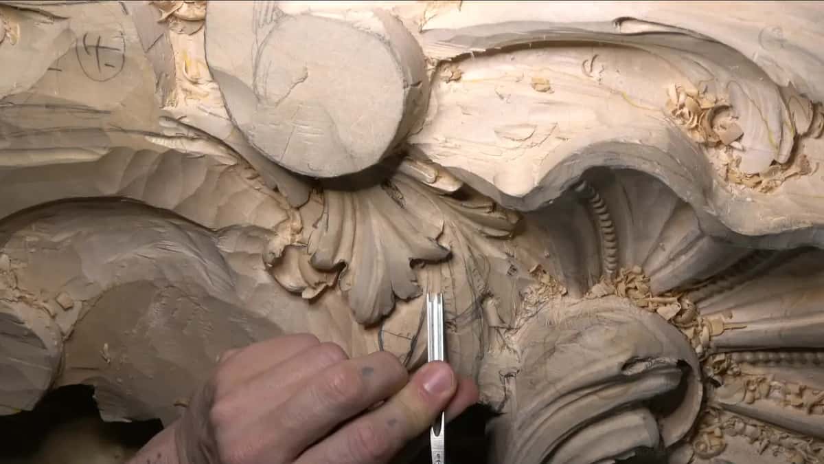 A narrow gouge held between thumb and fingers works the small fan leaf right below the round boss.