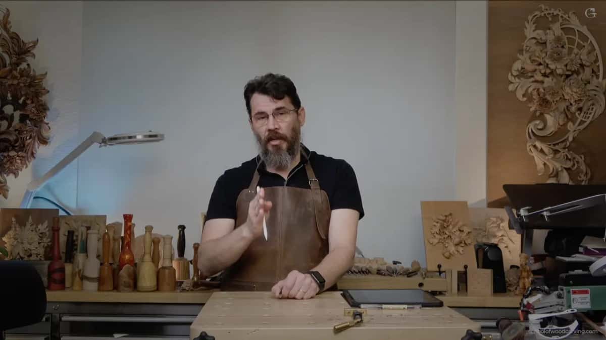 Alexander in a leather apron at his bench with his own carved panels hung on the walls