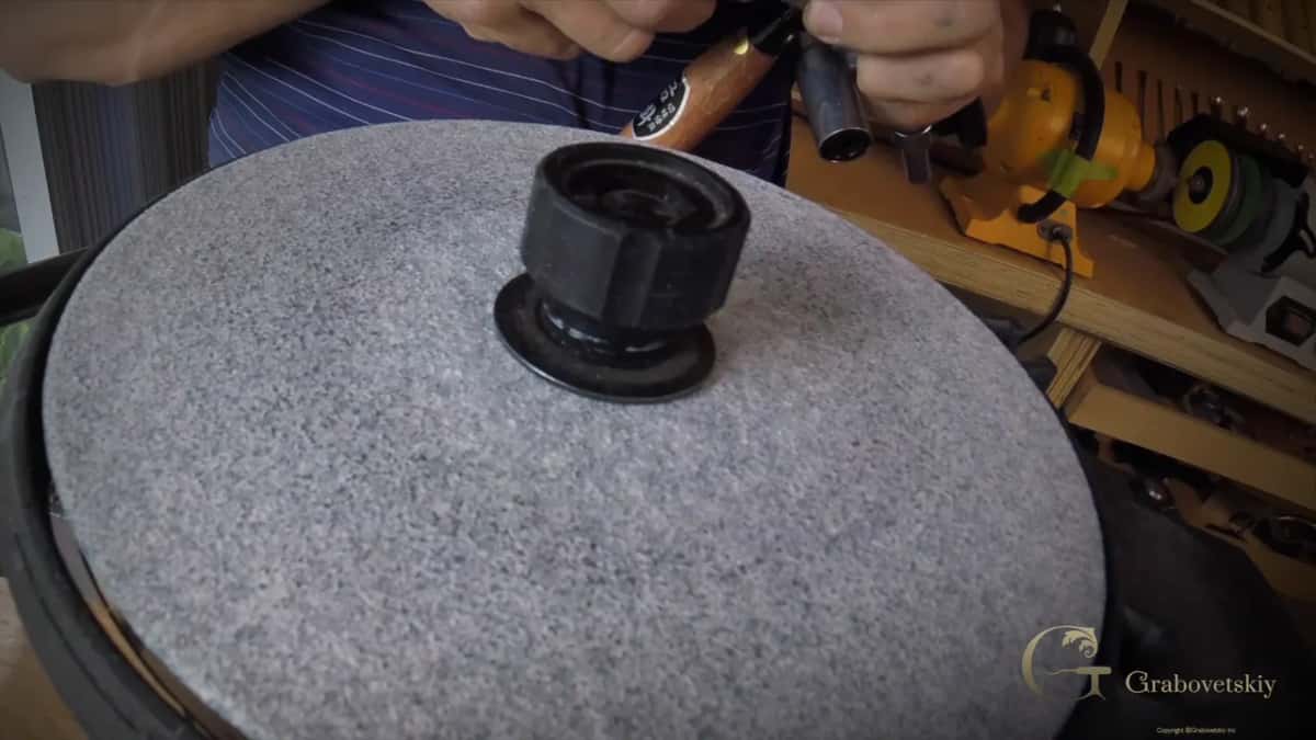 Grey abrasive on the machine, with a bench grinder and its coloured wheels behind on the shelf.