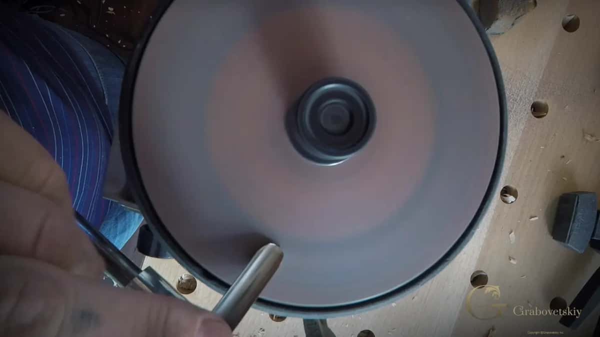 Steel meets the pink face at the very bottom of the wheel while a hand steadies it from the left.