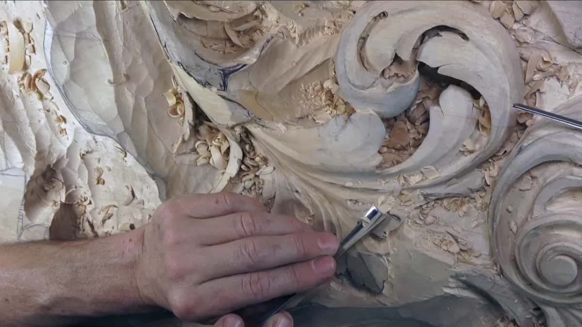 Pressed down by one hand, a short gouge with a bright ferrule bites into a lobe near the shavings.