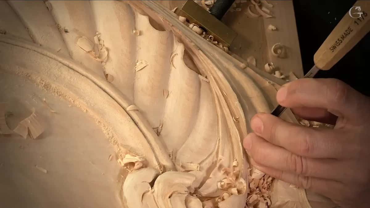 Close on a thin tool at the curled end of the shell, chips piled below