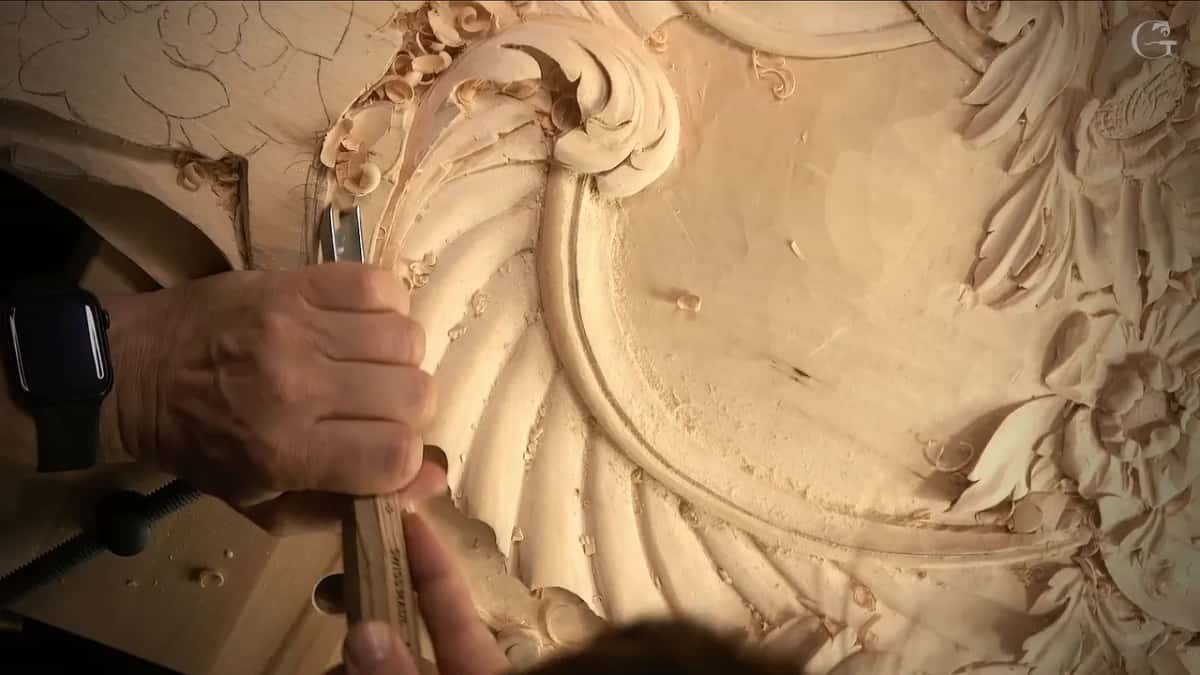 A wrist with a black watch, the gouge set upright at the curl of the scroll