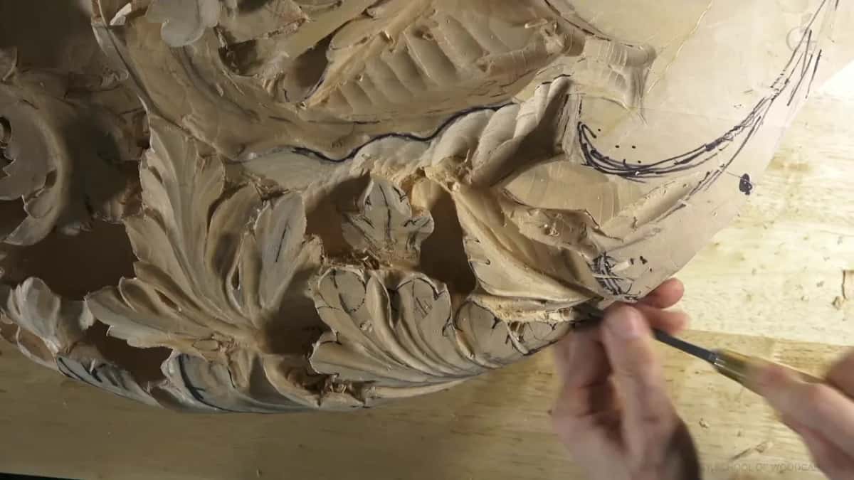 One side ahead of the other Right hand brings a thin tool along a leaf outline while the left of the panel sits much further along in deeper relief