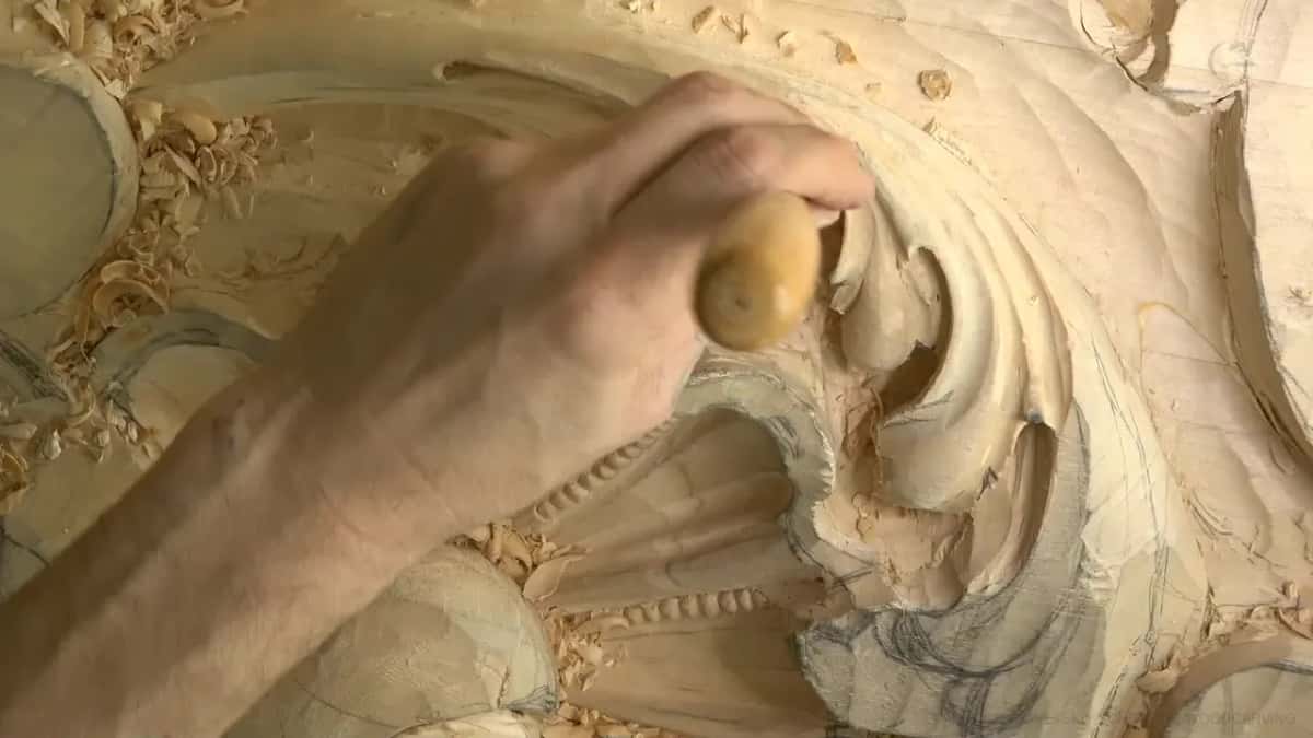 Pale round handle pressed down, the gouge edge buried in a curled lobe beside chips and pencil marks.