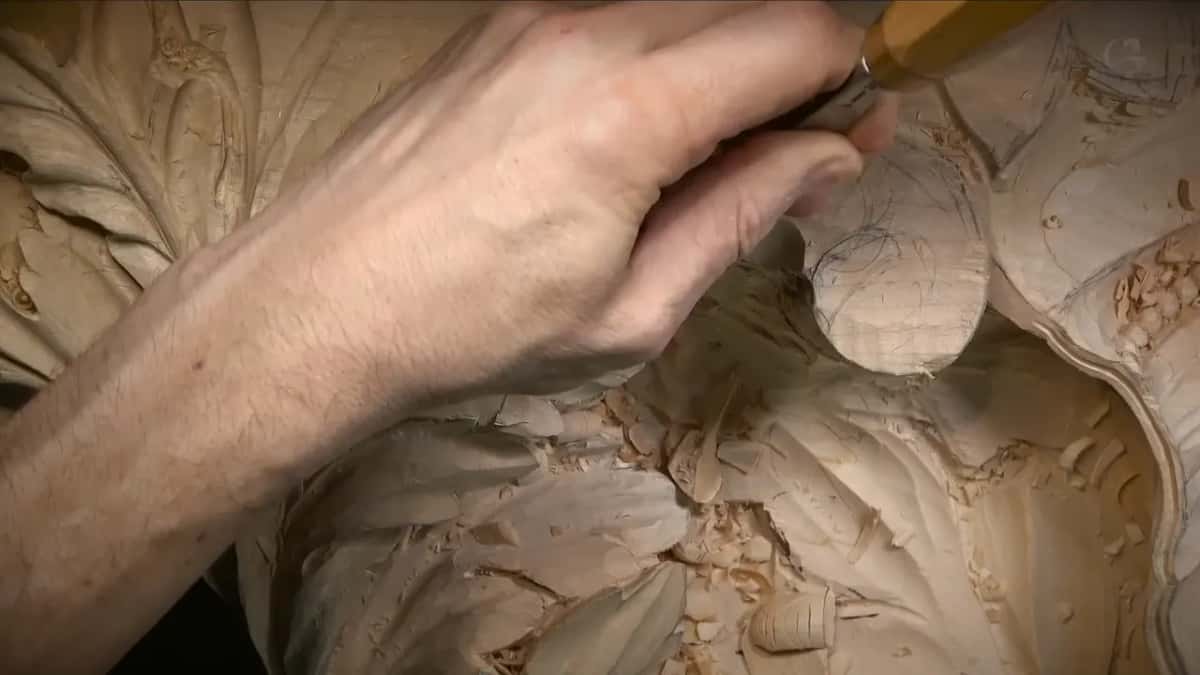 Knuckles over a gouge sunk into a round lump marked in pencil, shavings piled beneath
