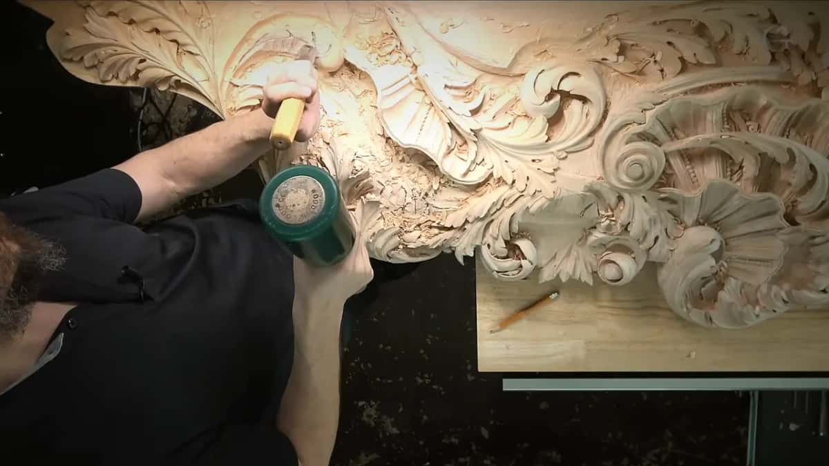 From above, the carver works a green mallet near the far end of the panel