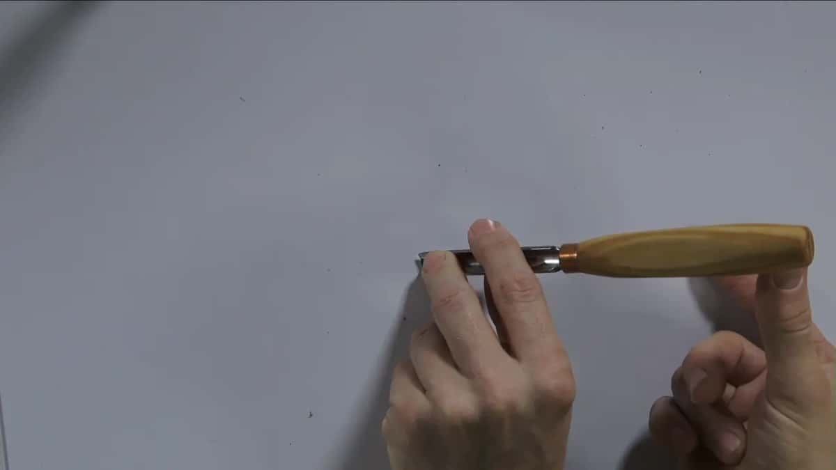 Both hands press a gouge flat to the bench.