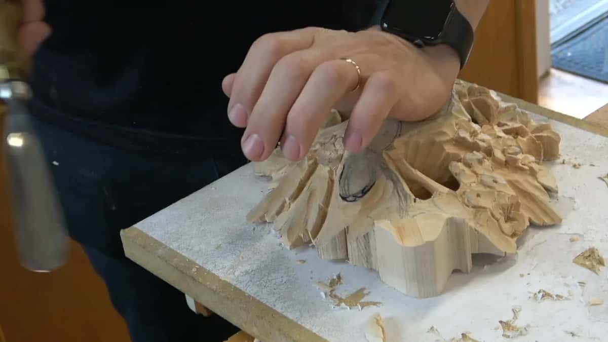 Both hands flat on the carving, holding it steady on the bench without a clamp anywhere near it