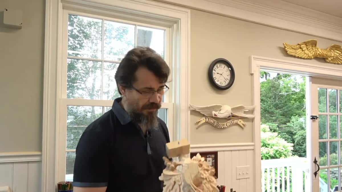 Alexander in the Maine workshop, a clock on the wall and gilded carvings mounted over the doorways behind him