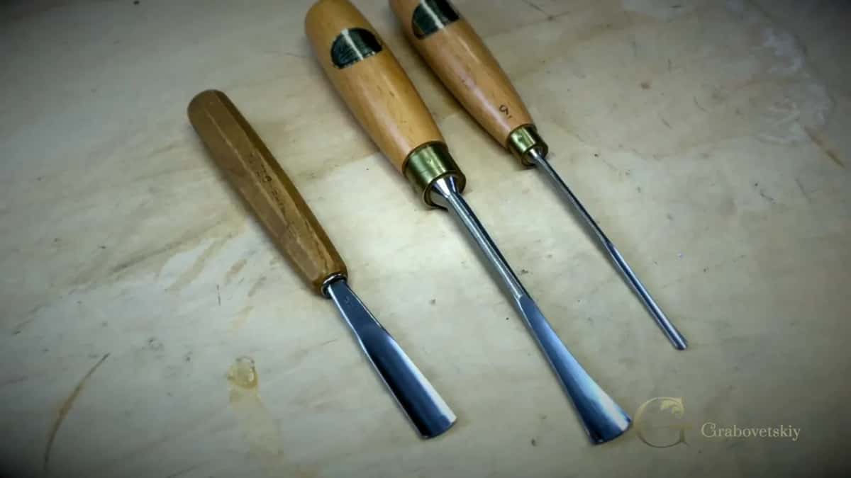 Three gouges laid out, one with a long plain handle and two with darker tips.