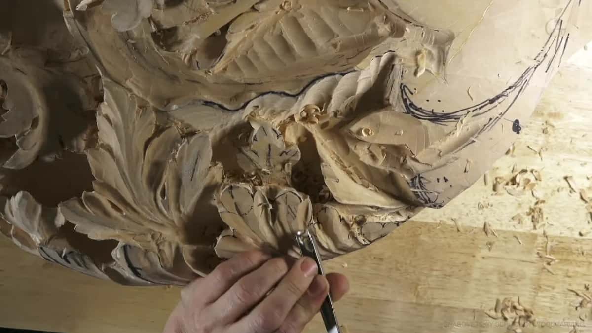 Both hands steady a gouge between two carved acanthus leaves near the rim.