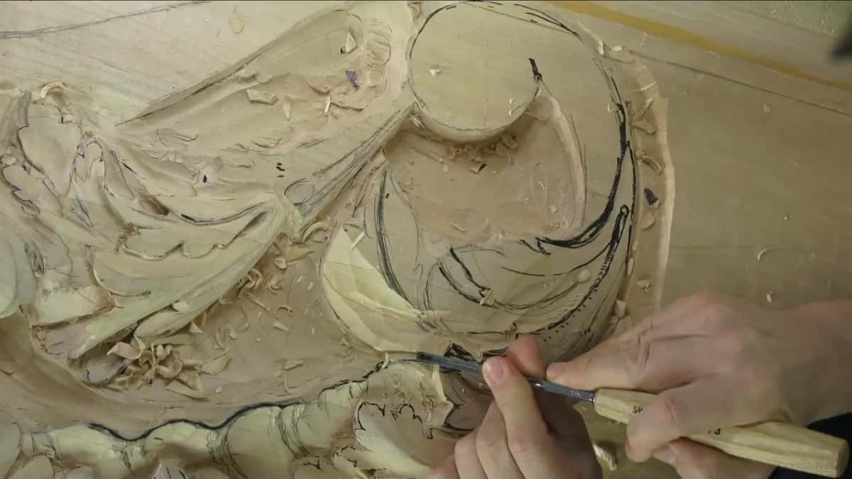 Two hands on one gouge along the lower curve of a scroll.