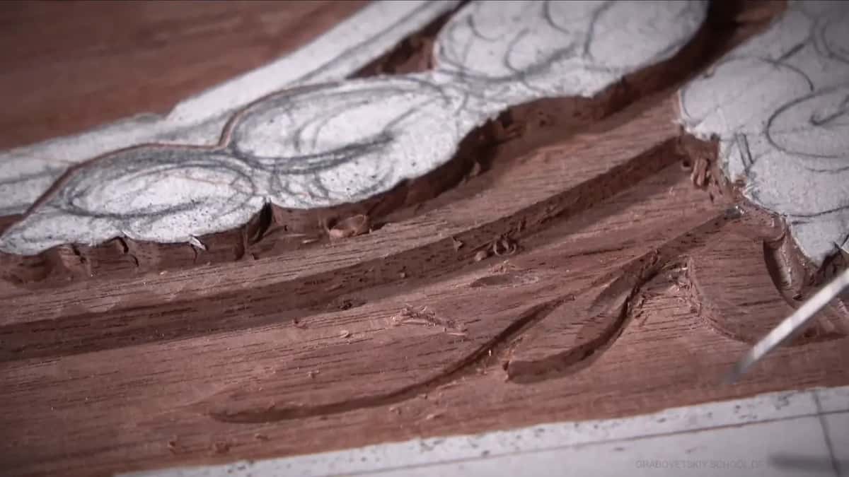 Steel tip entering at the right of the frame where a carved leaf edge meets open background