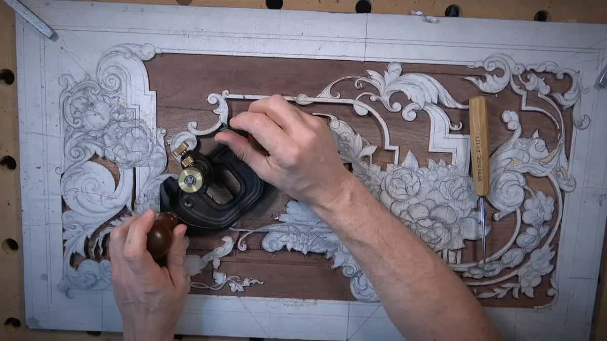 Router plane held in both hands, a Swiss Made handle lying on the board at right