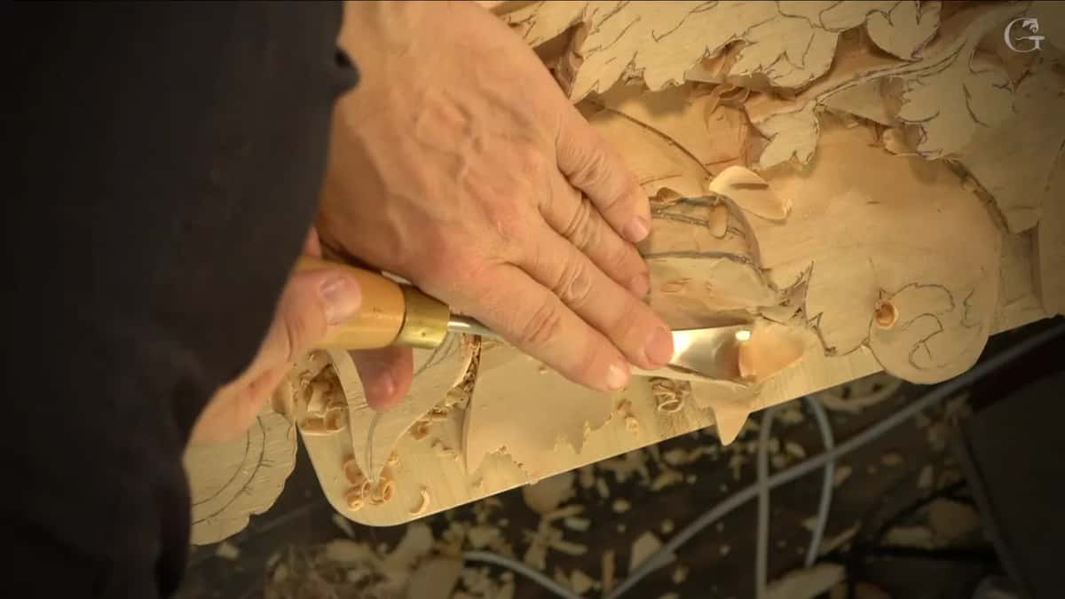 A wide gouge scoops a long hollow under a leaf as one hand presses the steel.