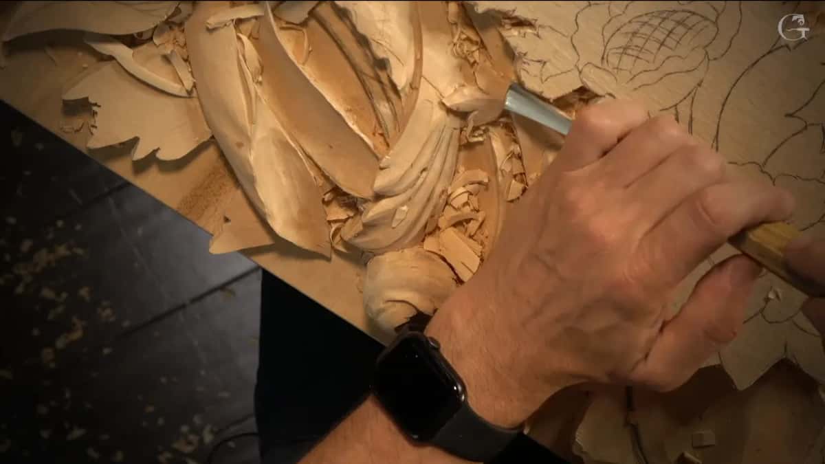Seen from above, a yellow handled gouge leans into the carved leaves.