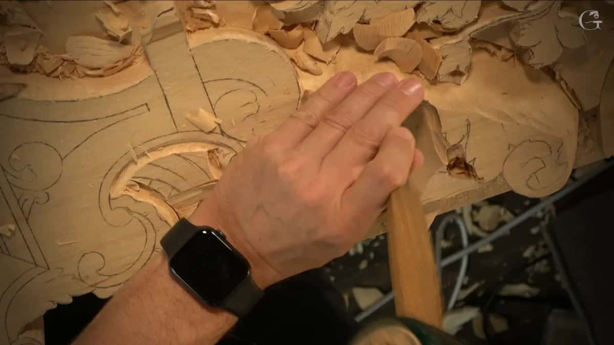 One hand presses a gouge down at the edge of a lowered hollow.