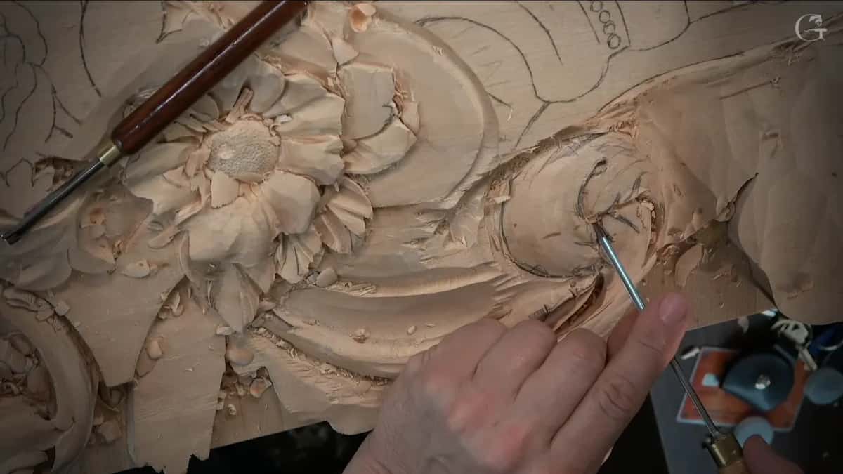 A thin tool stands in the eye of the scroll while a dark handled gouge rests across the flower