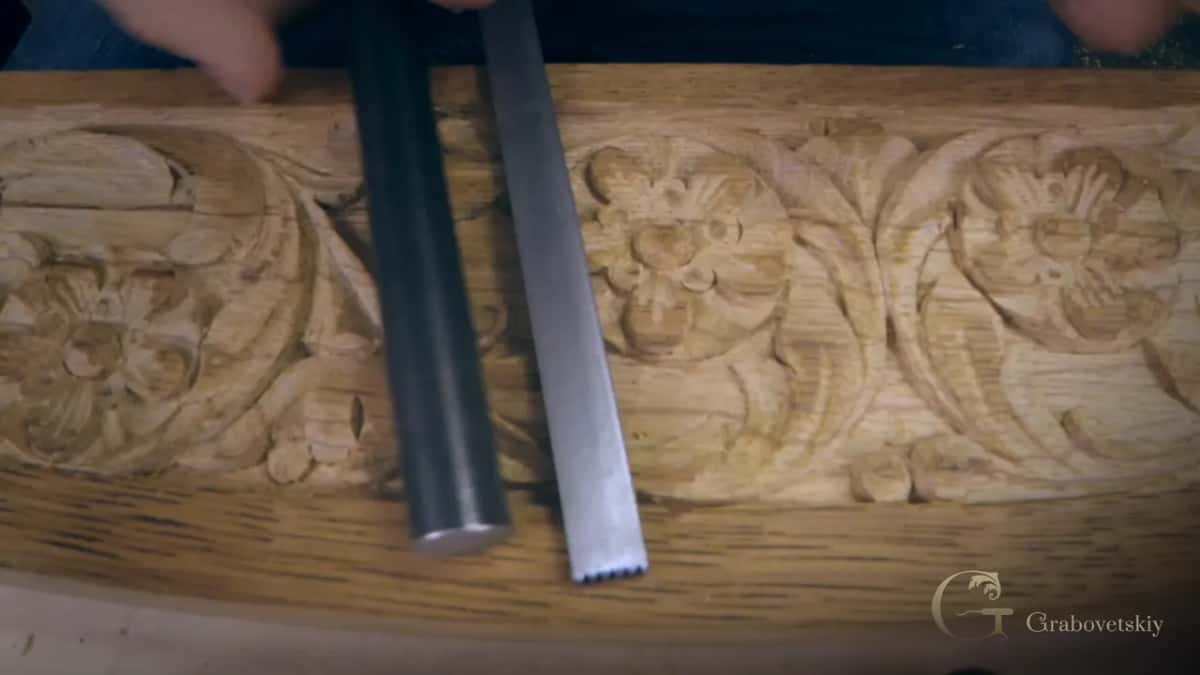 Two steel punches lying across the carved strip, one round and one with a toothed end