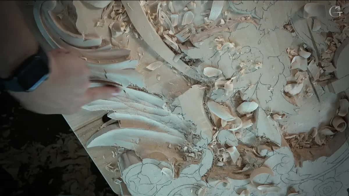 A hand rests at the edge of the carved leaves while curls of shavings cover the drawing beside it