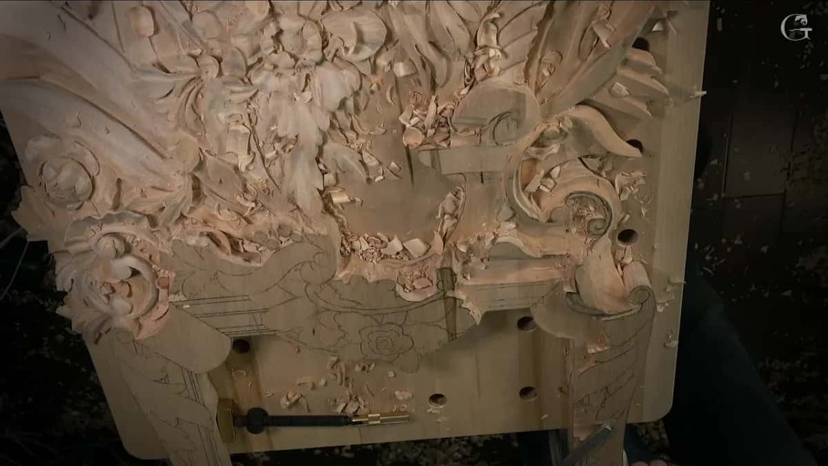 The whole carved panel standing at the bench, flowers above and a tool lying below it