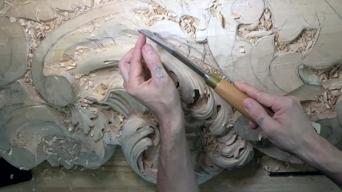 Left fingers guide a long narrow blade laid almost flat on a carved scroll.