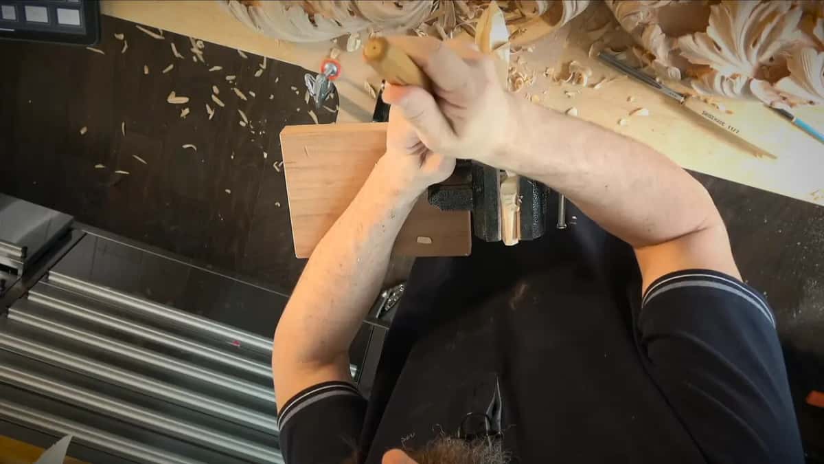 Held by the waste Arms over the bench, one hand on a gouge handle, shavings everywhere