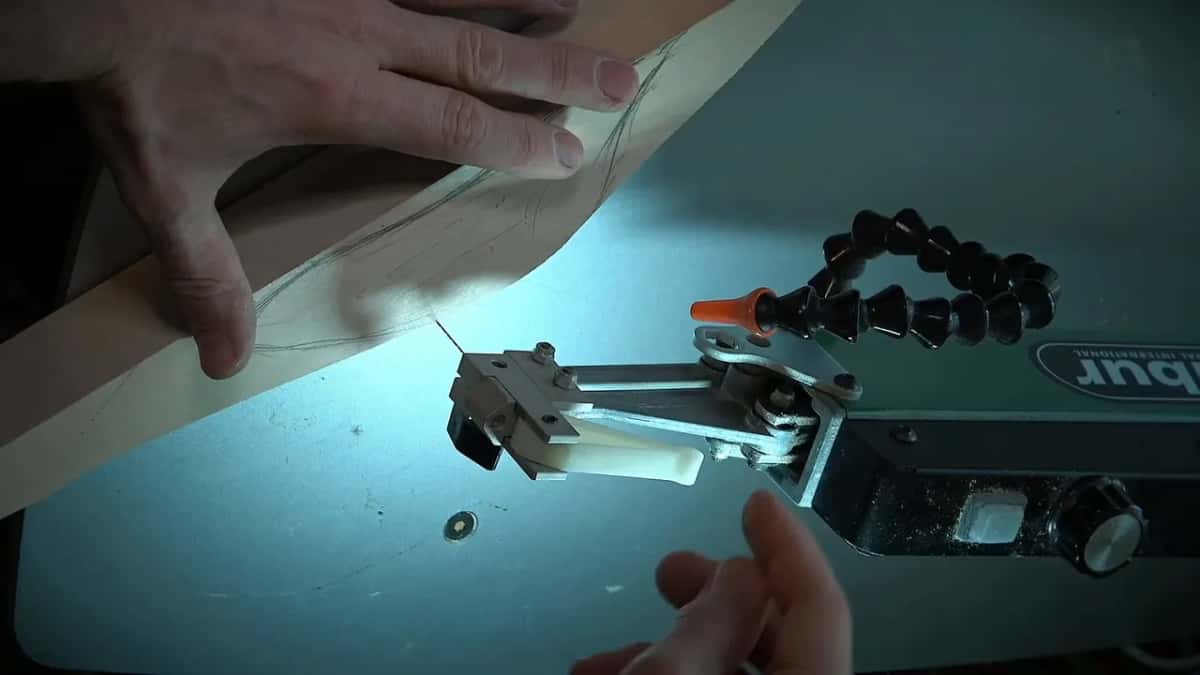 The scroll saw Scroll saw table under its lamp, blade and hold down set, hands feeding a marked blank