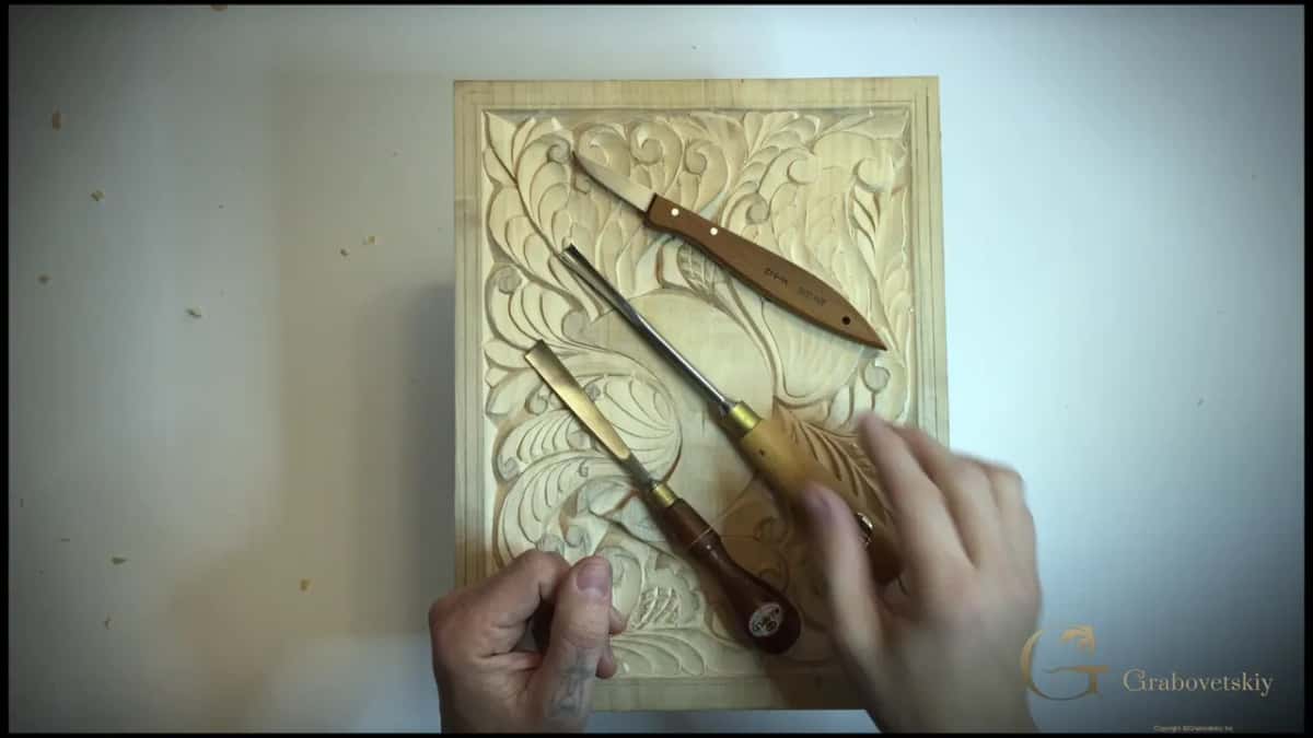 Knife and gouge lying together on the panel, one straight edge and one with a sweep, the whole difference in a photograph.